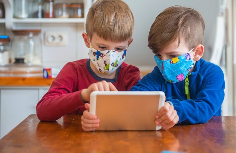 ابتلا کودکان به کرونا در کانادا- دو کودک ماسک زده در حال کار با تبلت
