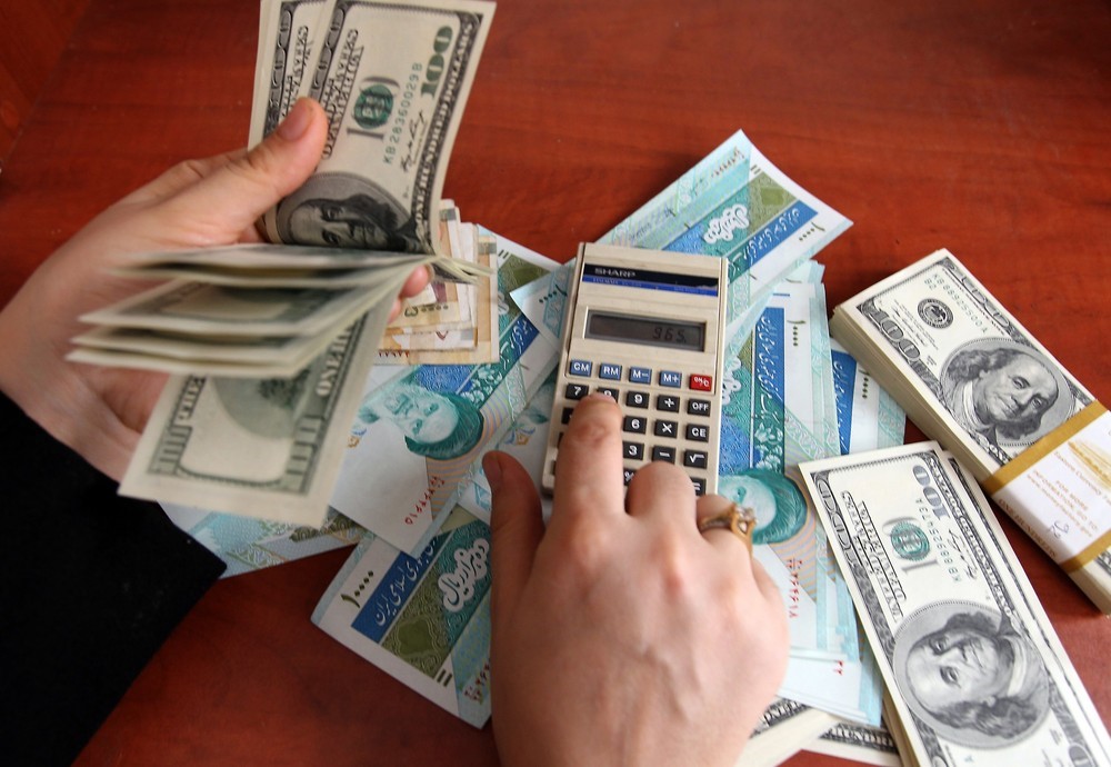 قيمت دلار- فردی ماشین حساب در دست در کنار اسکناس های دلار و هزار تومانی