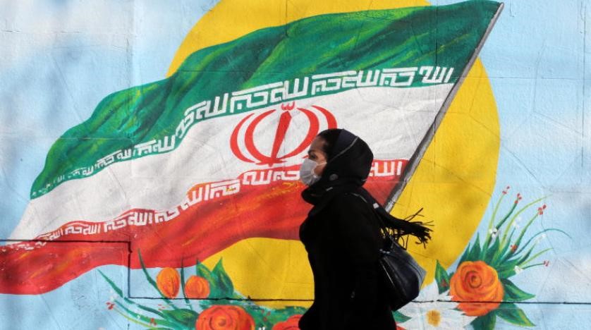 واکسن کرونای ایرانی- زنی ماسک زده در حال عبور از کنار دیواری با نقاشی پرچم ایران