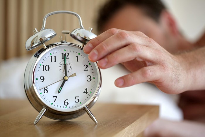 زمان خواب - فردی خواب آلود درحال خاموش کردن زنگ ساعت